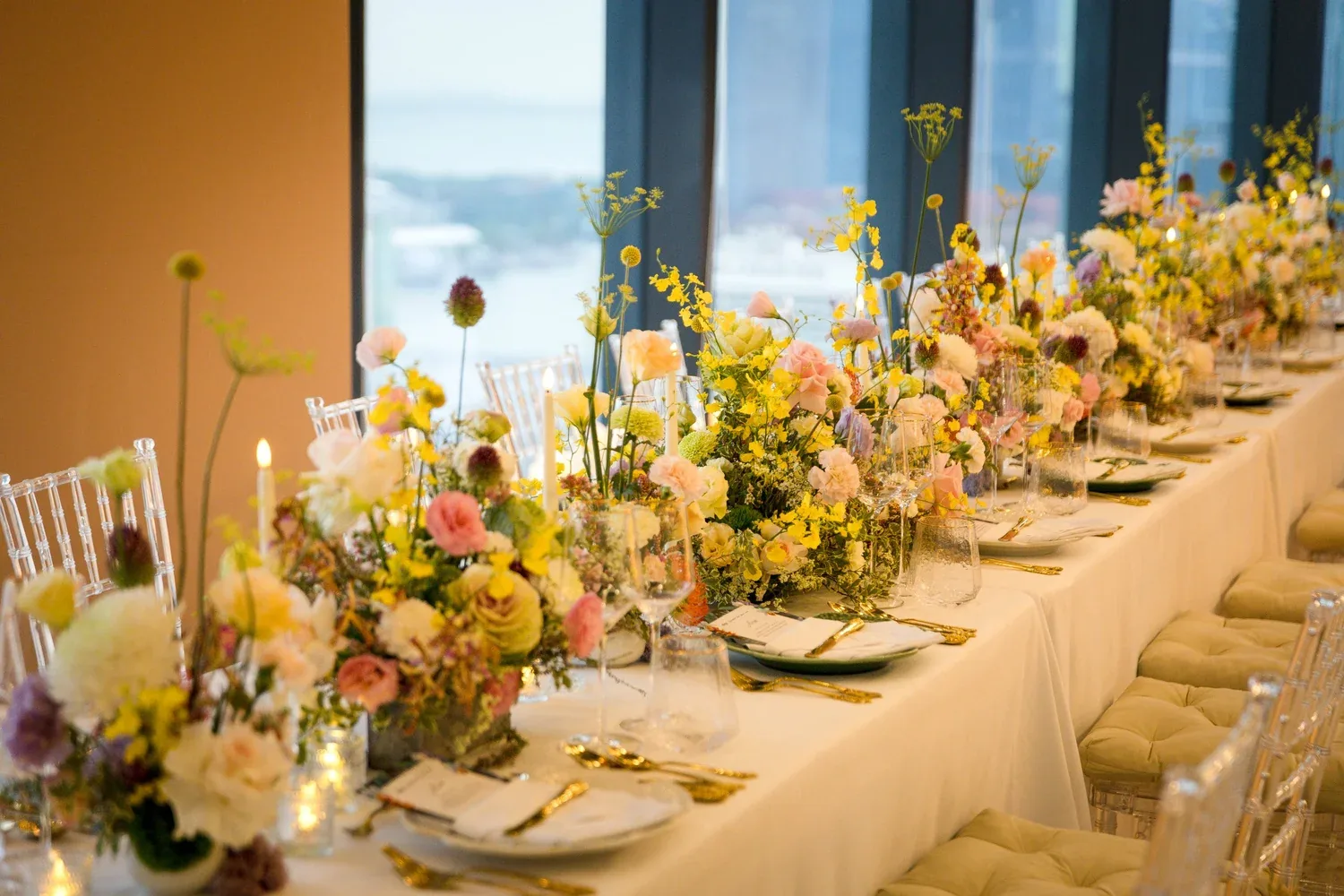 Golden floral long-table styling beside full-height windows
